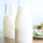 Homemade ranch dressing with greek yogurt in two long neck salad dressing jars.