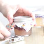 Securing a breathable cover onto a jar of solid air freshener.