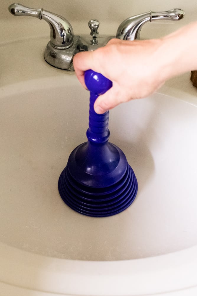 Using a plunger to help unclog the bathroom sink.