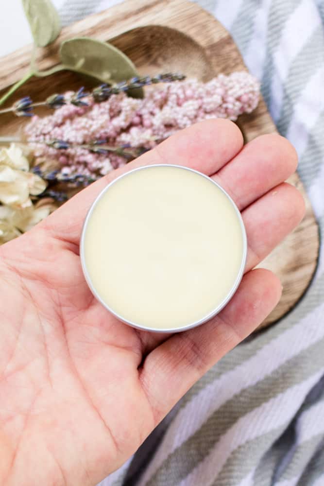 Holding a solid perfume container with dried lavender and flower buds in the background.