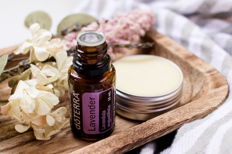 Perfumes, lavender essential oil, dried flowers and lavender springs on a wooden storage tray.