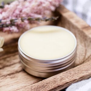 A solid perfume in a small metal tin stored on a wooden shelf.