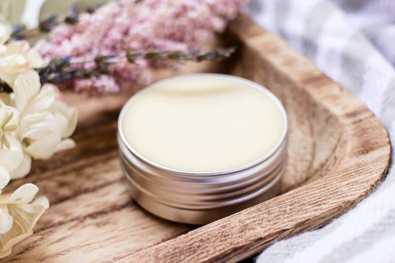 A solid perfume in a small metal tin stored on a wooden shelf.