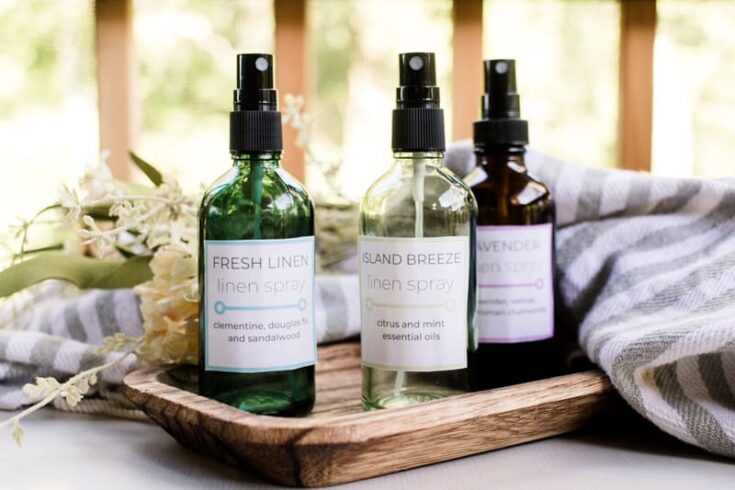 Homemade linen sprays scented with essential oils on a wooden tray with homemade labels.