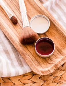 A DIY blush cream in a small metal tin with a wooden applicator brush.