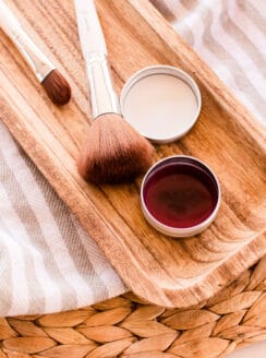A DIY blush cream in a small metal tin with a wooden applicator brush.
