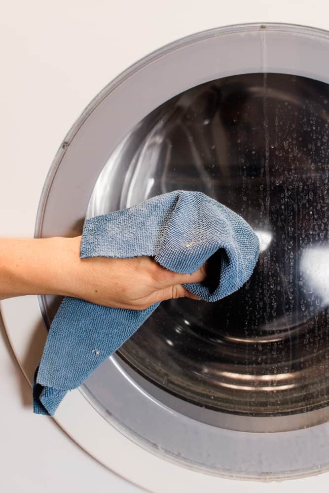 Wiping down a mildewy smelling washing machine with a clean cloth.