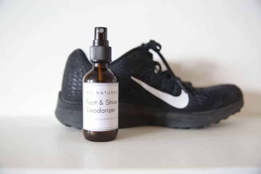 DIY foot deodorizer spray in a glass bottle in front of athletic shoes.