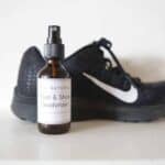 DIY foot deodorizer spray in a glass bottle in front of athletic shoes.