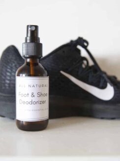 DIY foot deodorizer spray in a glass bottle in front of athletic shoes.