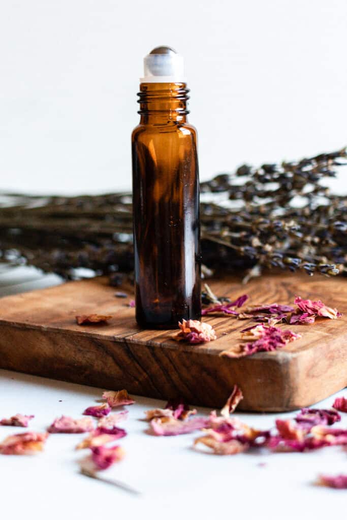 Essential oils for anti aging roller bottle on a wooden holder with dried flowers.