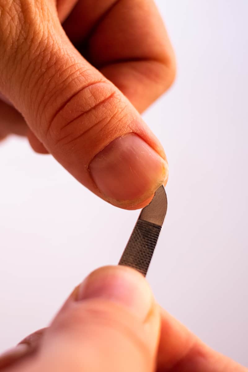 Removing dirt from underneath the fingernails with an under nail cleaner. 