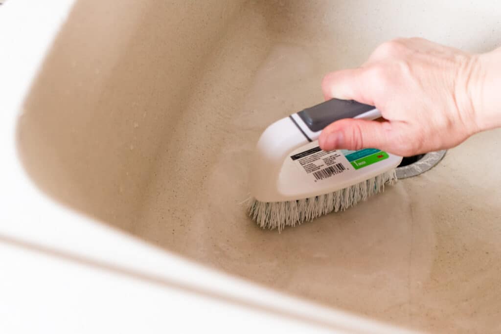 Using a nylon scrubbing brush to clean a composite sink. 