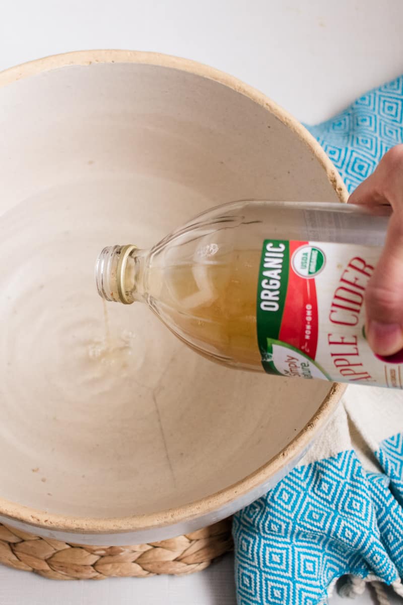 Adding vinegar to make baking soda vinegar foot soak in a large bowl. 