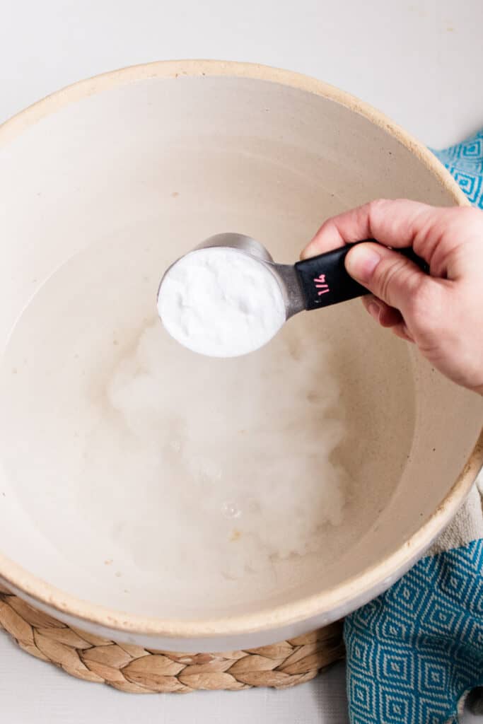 Adding baking soda to the warm water in a foot basin.