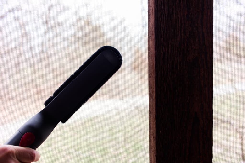 Vacuuming the outside of  of a screen with an upholstery attachment to loosen up the dirt and pollen.