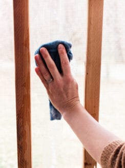 Scrubbing down a porch screen with dish soap and a wet cloth.