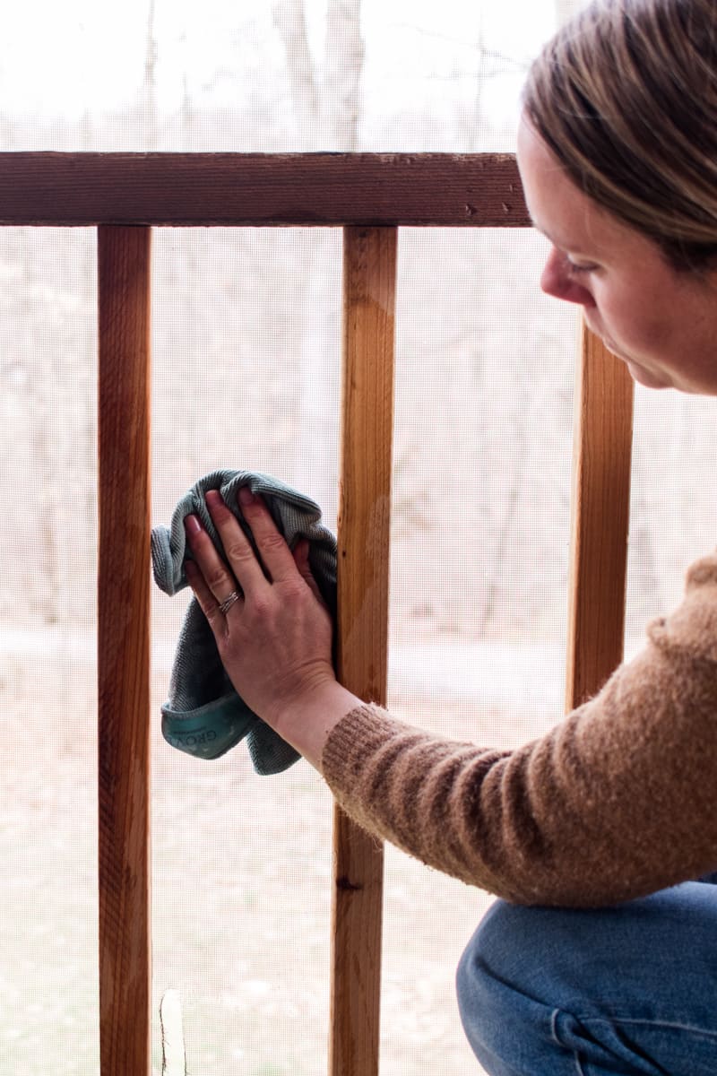 Cleaning a porch screen with a wet rag. 