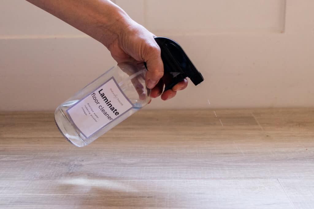 Spraying floor shiner onto gray laminate flooring.