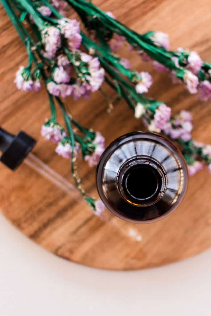 Glass jar of cleansing oil on a wooden tray.