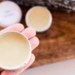 Holding a small tin of vegan lip balm for soothing chapped lips.