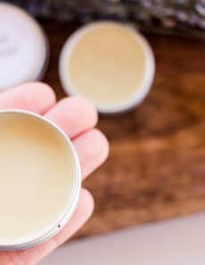 Holding a small tin of vegan lip balm for soothing chapped lips.