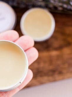 Holding a small tin of vegan lip balm for soothing chapped lips.