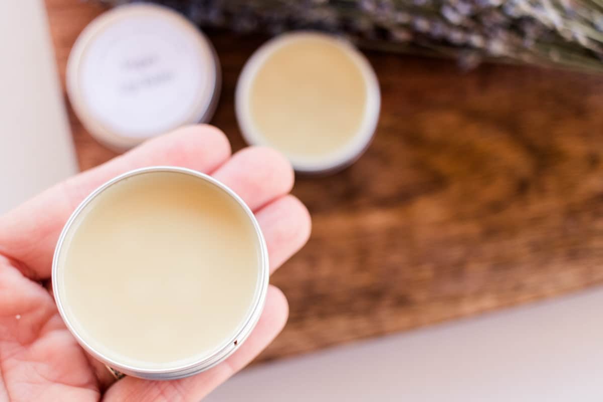 Holding a small tin of lip balm.