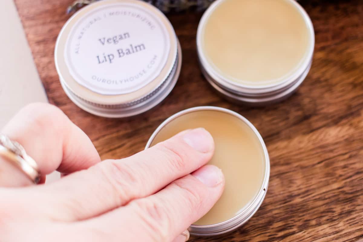 Dabbing two fingers into a vegan lip balm tin.