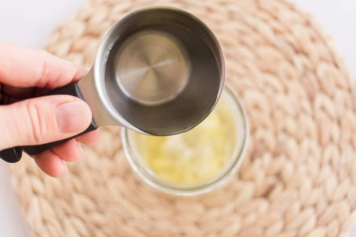 Pouring the melted conditioner ingredients into a tall mason jar.