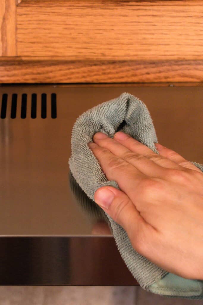 Wiping the grease off a range hood with a homemade cleaner and a clean cloth.
