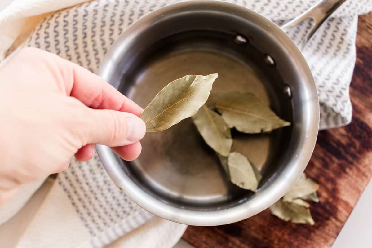 Adding bay leaves to water in a pan. 