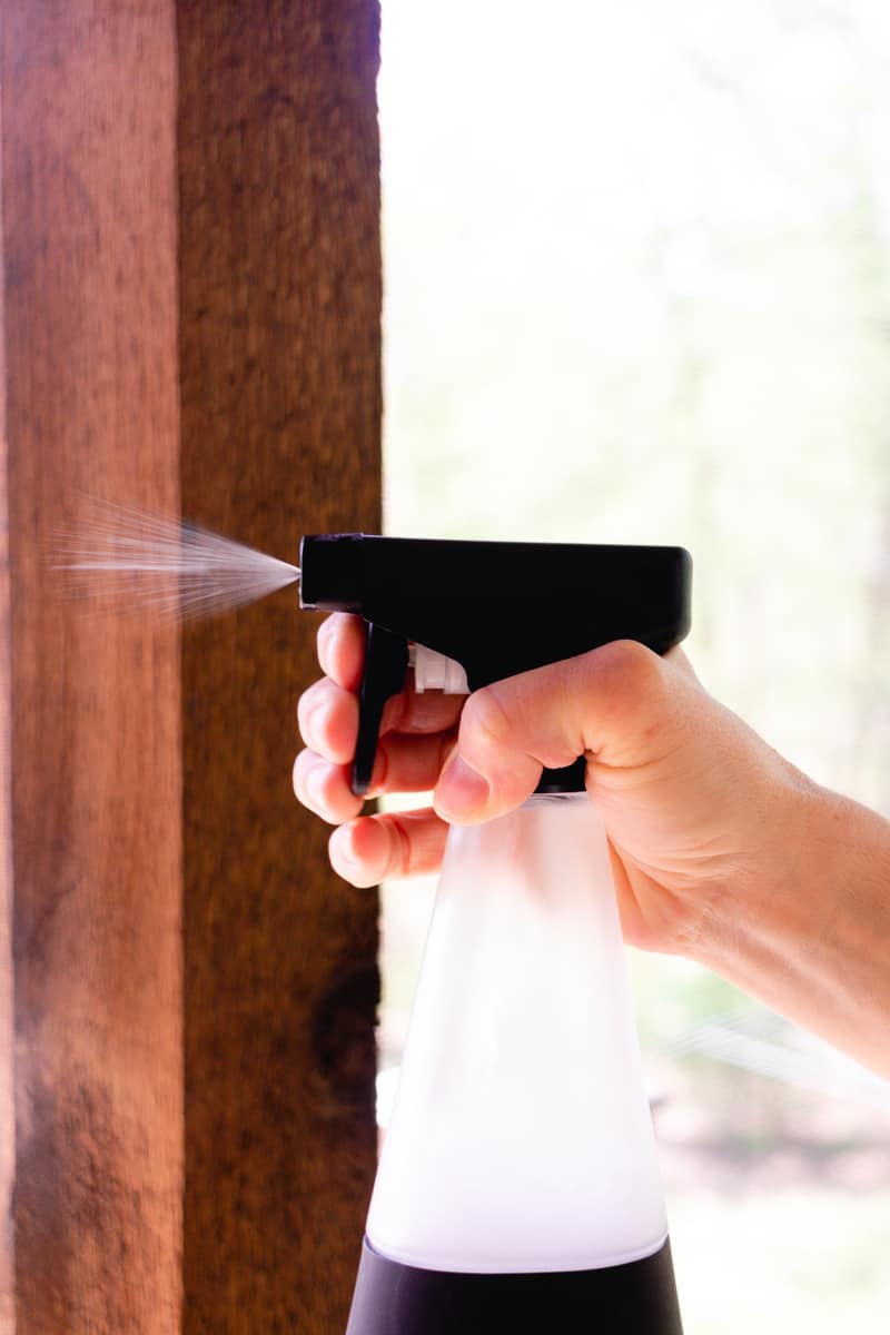 Spraying wasp spray onto porch screens to keep them away.