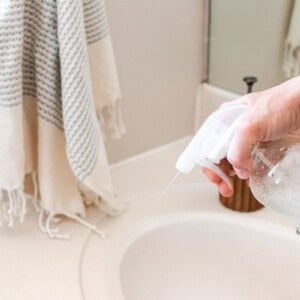 Spraying a homemade bathroom surface cleaner onto a bathroom vanity.