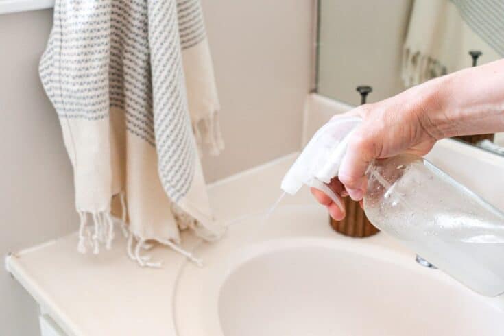 Spraying a homemade bathroom surface cleaner onto a bathroom vanity.
