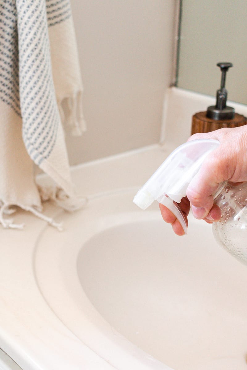 Spraying homemade bathroom cleaner on bathroom surfaces. 