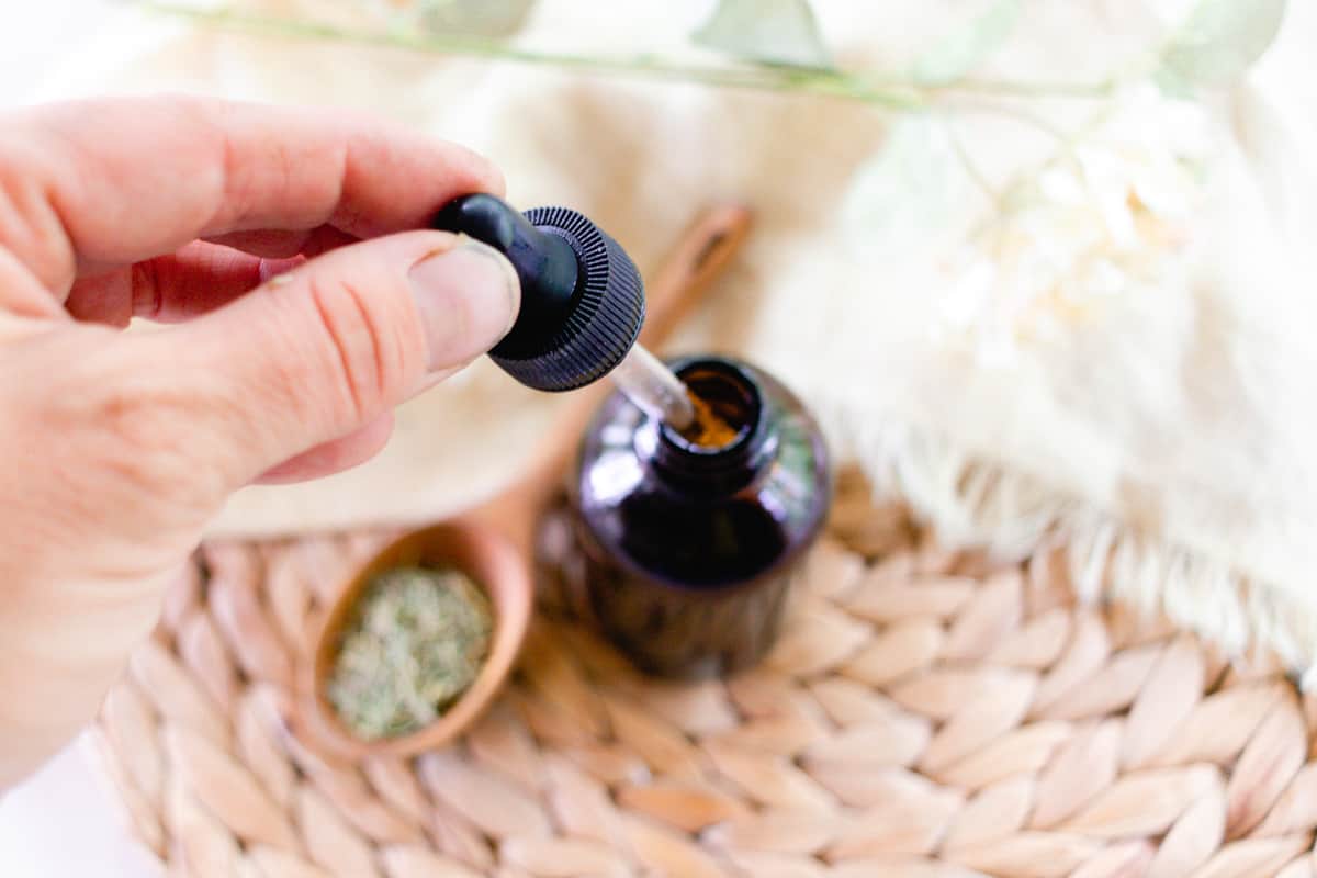 Adding the homemade rosemary oil to a glass jar for storage.