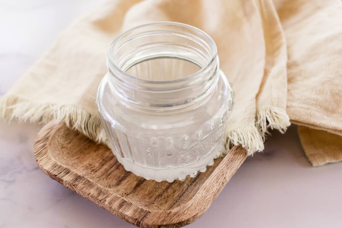A jar of melted coconut oil on a wooden tray.