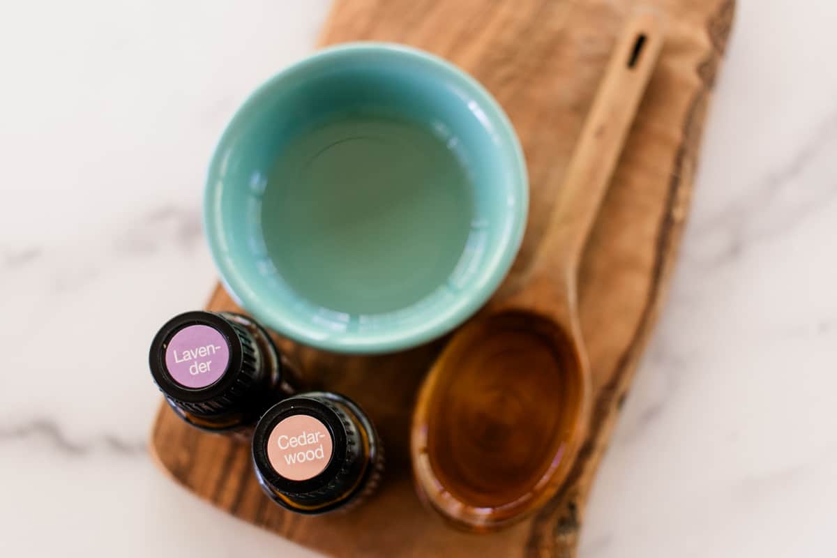 Tanning oil ingredients in a small blue bowl with a measuring spoon and essential oils.