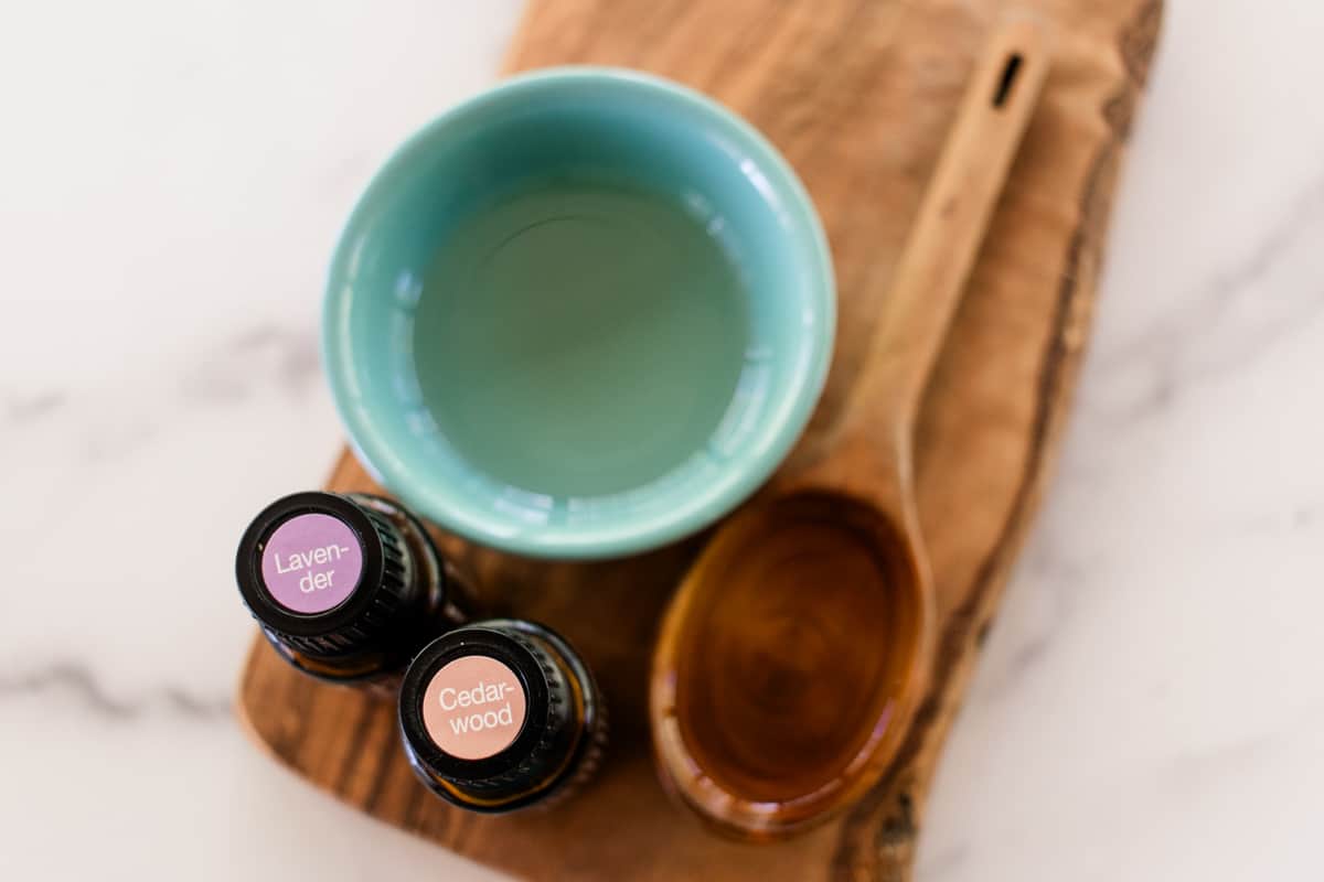 A small bowl of the homemade tanning oil with fragrance ingredients sitting on a wooden tray with a mixing spoon.
