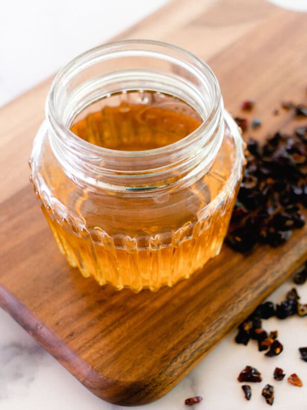Homemade rosehip oil in a glass jar with dried rosehips next to it.