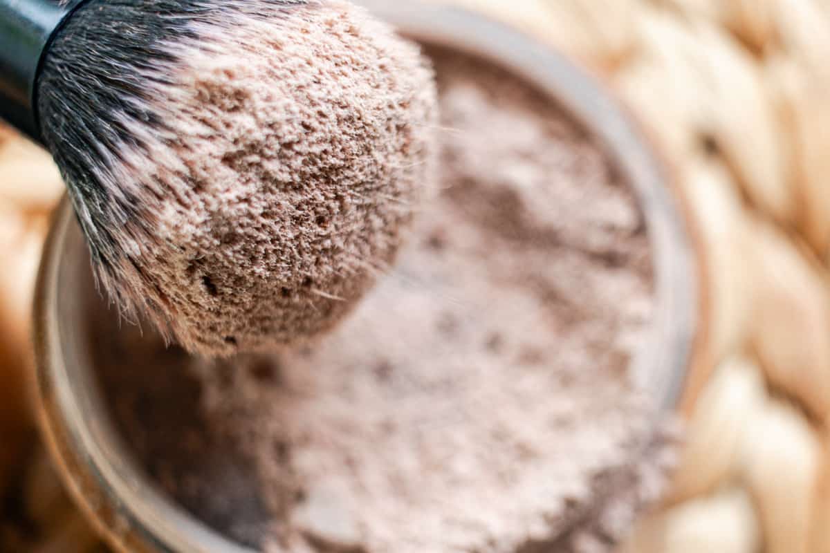 A makeup brush with cornstarch powder being tapped against the side of a container.