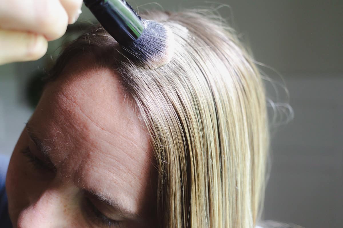 Dabbing the cornstarch dry shampoo into the hair with a makeup brush.