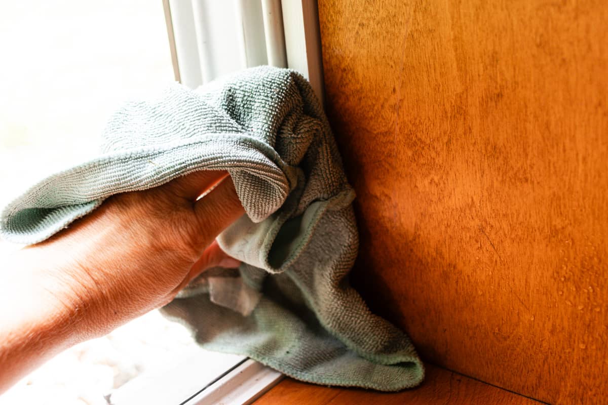 Wiping the moldy window sill with a clean cloth.