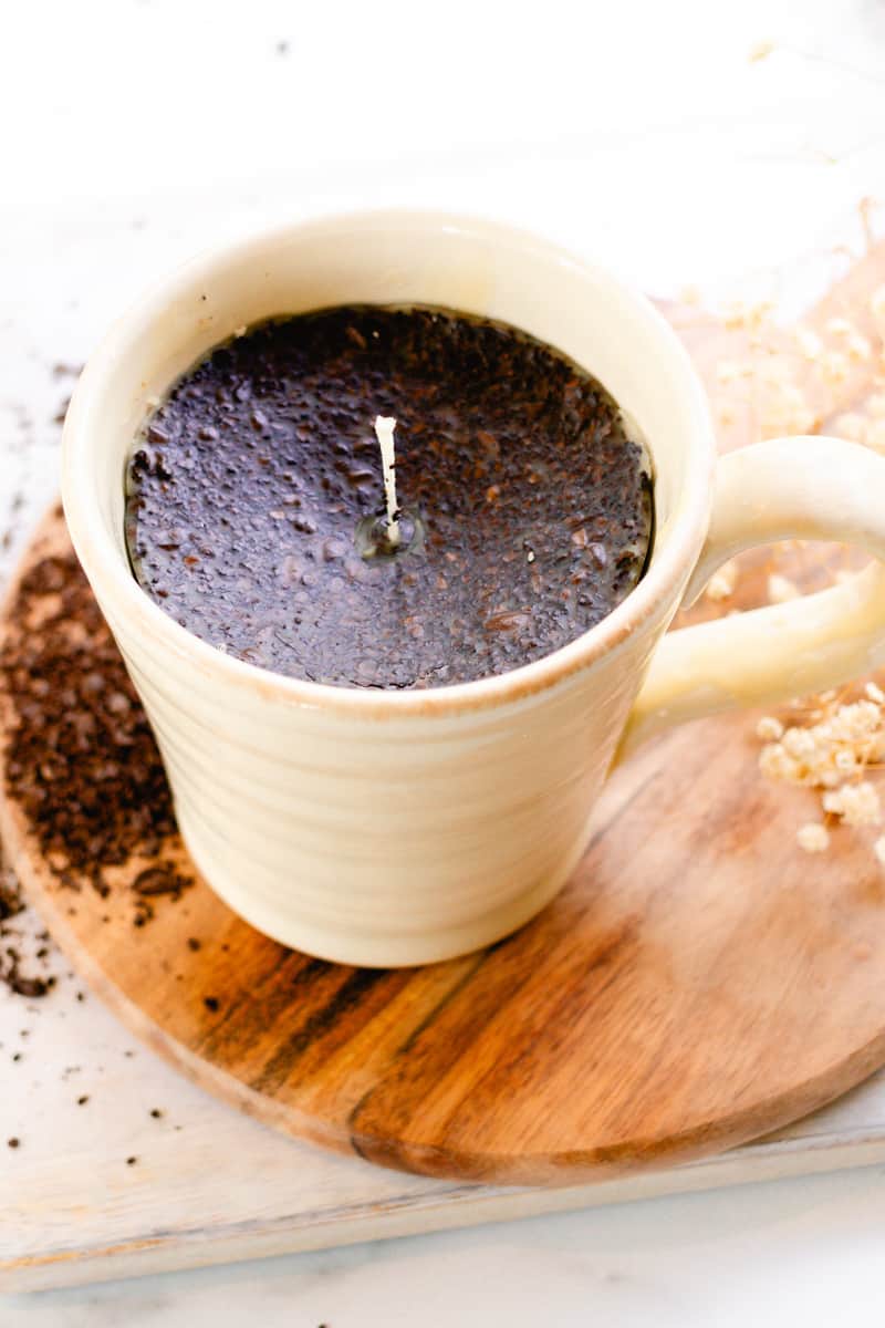 Coffee candle with fresh coffee grounds stirred into it on a wooden top.