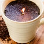 A coffee candle with coffee grinds in a coffee mug.