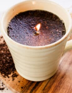 A coffee candle with coffee grinds in a coffee mug.