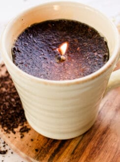 A coffee candle with coffee grinds in a coffee mug.