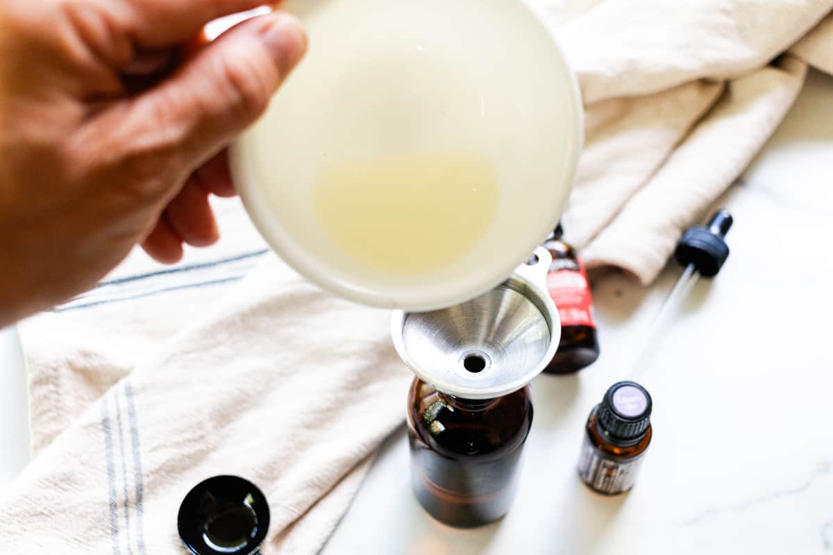 Pouring jojoba and rosehip oils into the face oil container using a metal funnel.