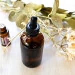 A homemade facial oil with an essential oil bottle and dried flowers in the background.